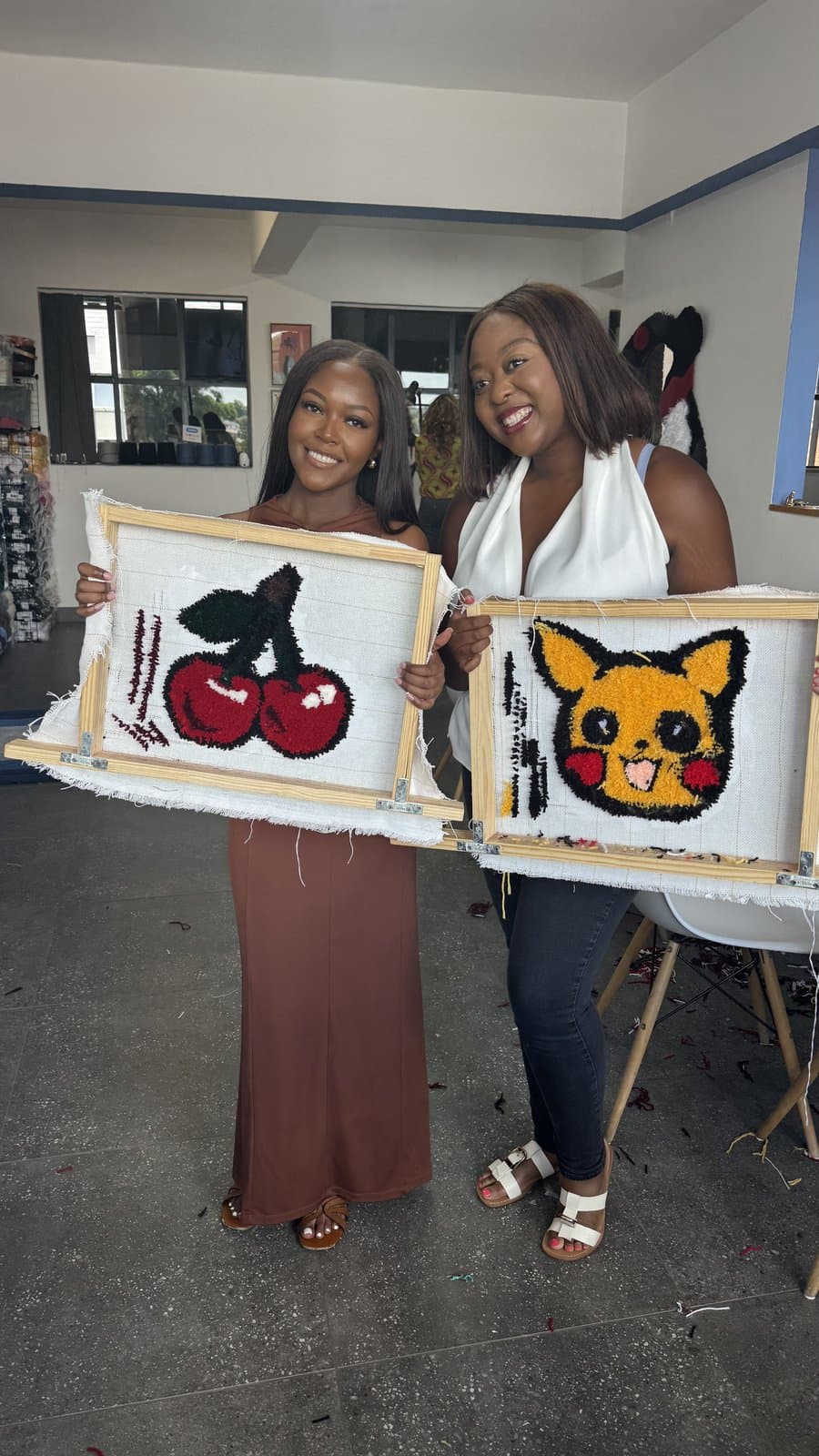 Two friends holding up their finished tufted rug pieces, a cherry design and a character design